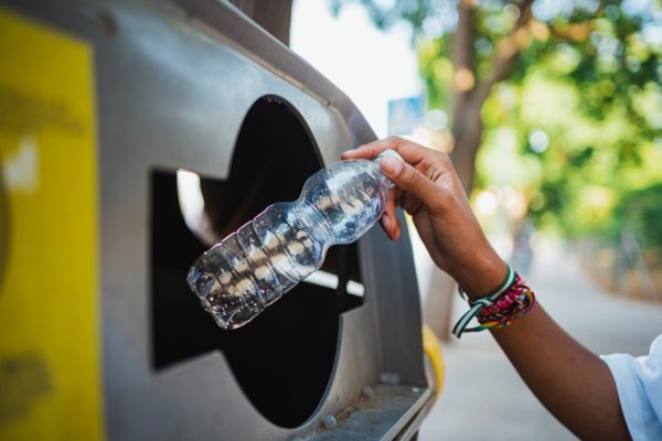 Close-up view of woman's hand recycling a plastic bottle. 