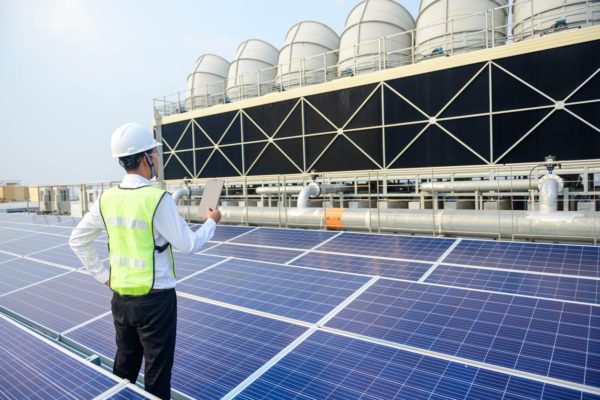 Worker inspects solar panels on industrial building roof. 