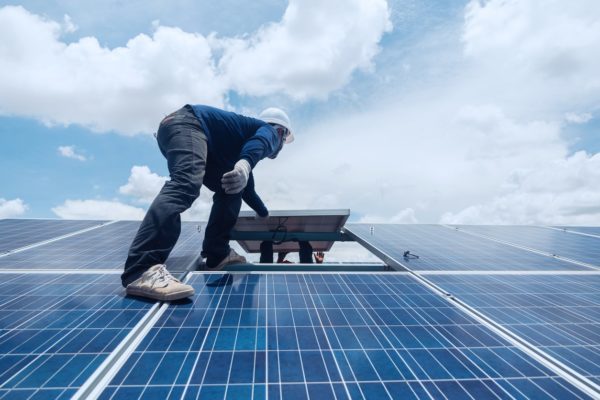 Closeup view of worker replacing a solar panel on the roof of a commercial building.