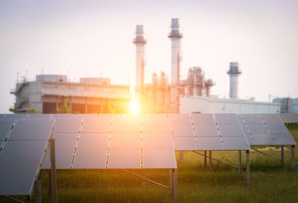 Sunset over ground-mounted solar panels in front of an industrial plant. 